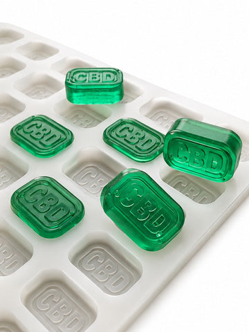 Side-angle view of a 4mL brick gummy mold with 185 cavities and translucent emerald green CBD gummies on a white background